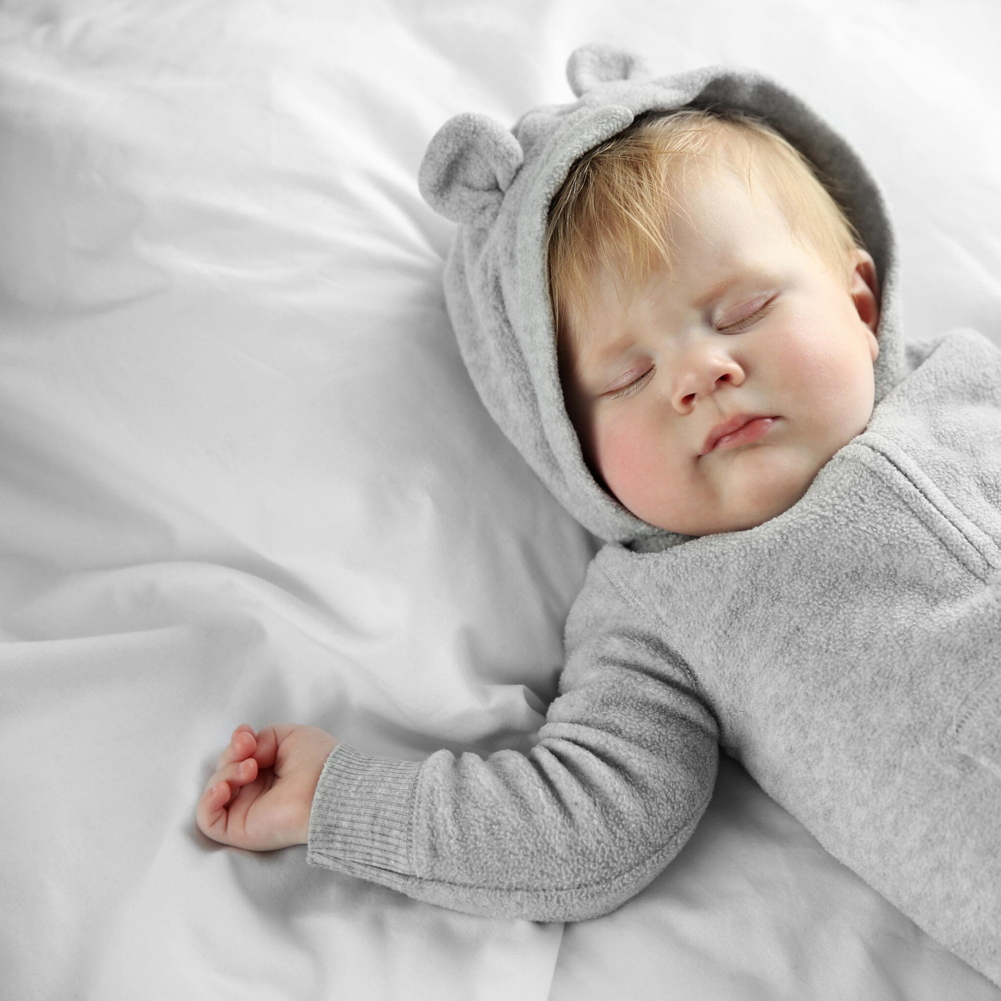 Little baby boy in grey pajamas sleeping on the bed